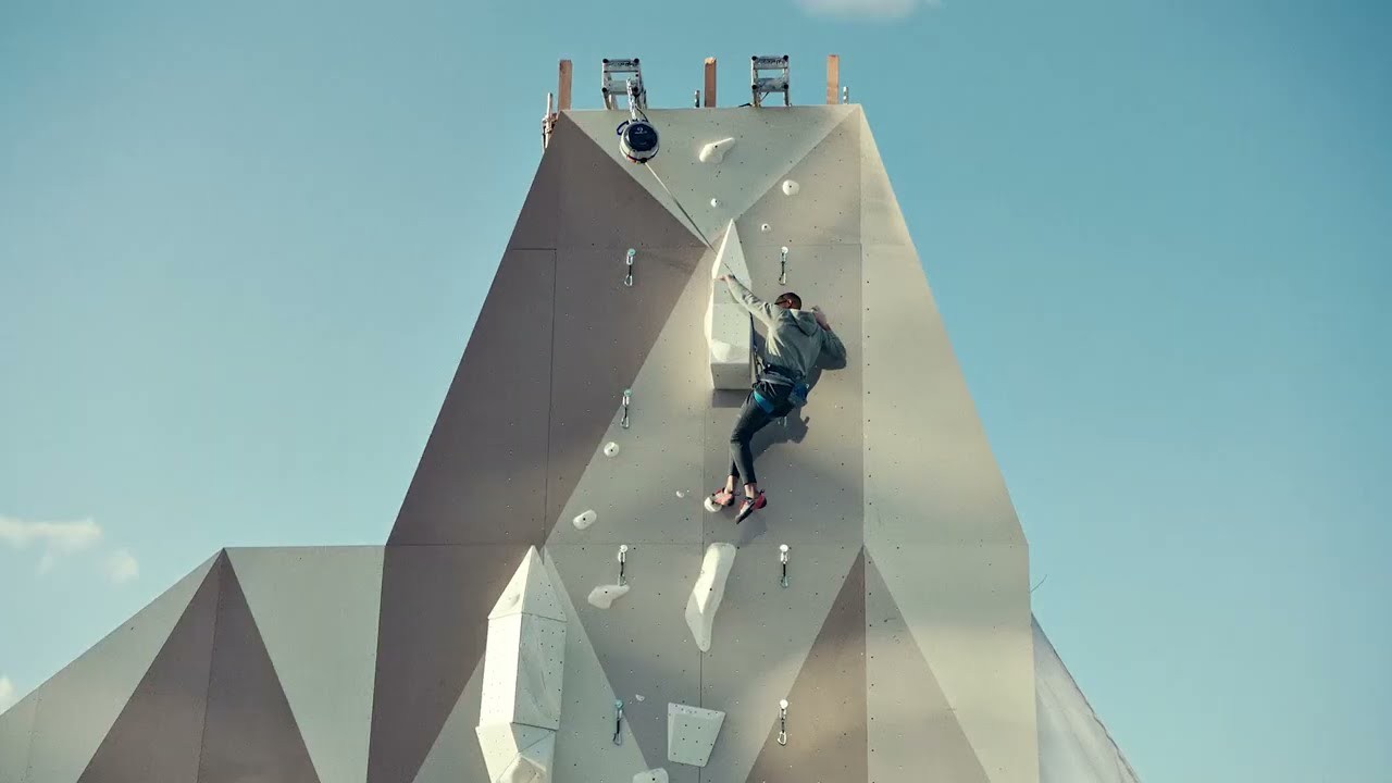 Still from “Got Milk? | The Wall” (May 18, 2021): a climber on a tall white climbing wall