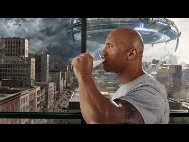Johnson drinks a glass of milk at the window, a flying saucer over the city behind him
